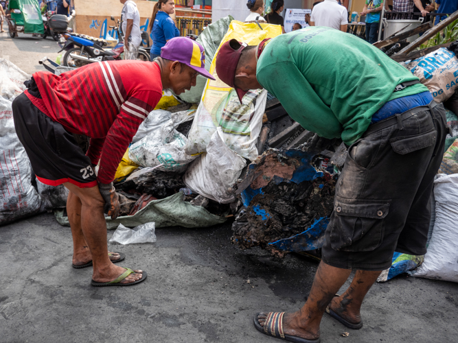Residents peer inside a bag of burned debris. 【Photo by Matt Serrano】
