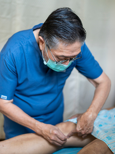 Dr. Jose Ramon “Chito” Guzman inserts a needle into a patient’s leg during the acupuncture session.【Photo by Harold Alzaga】
