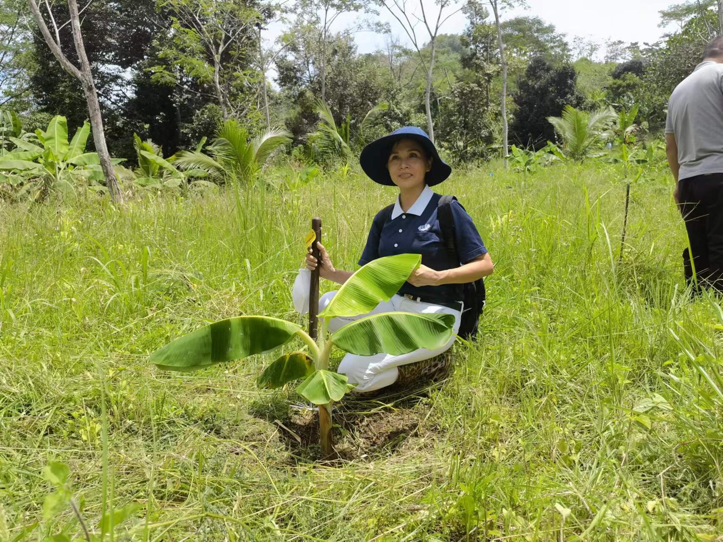 Volunteer poses for a phot with a growing banana tree, planted three months ago.