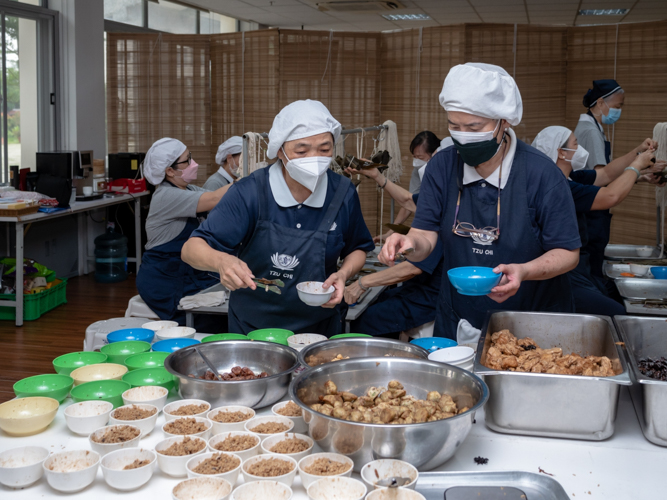  Volunteers place the sticky rice in bowls that will go to a group in charge of stuffing them into cone-shaped bamboo leaves.【Photo by Daniel Lazar】
