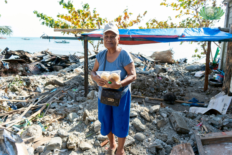 Linda Danao stands before what’s left of her house. Holding the bread that Tzu Chi volunteers gave her, she is grateful for volunteers’ visit and willingness to help. 