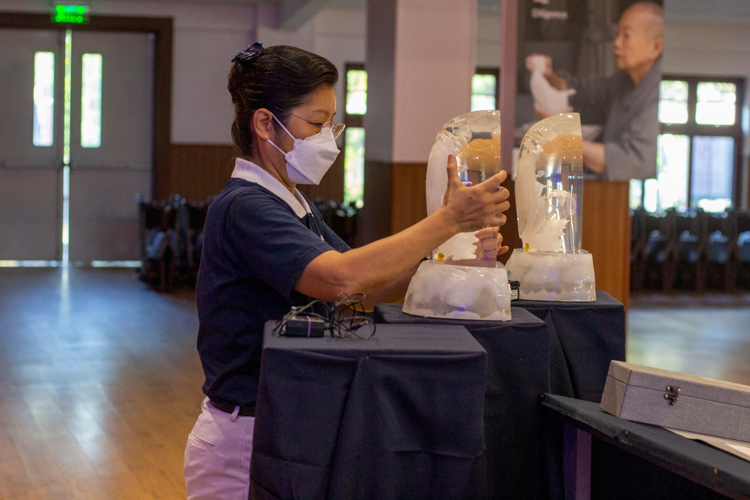 A volunteer places a crystal Buddha on a stand at the Jing Si Auditorium. 【Photo by Matt Serrano】