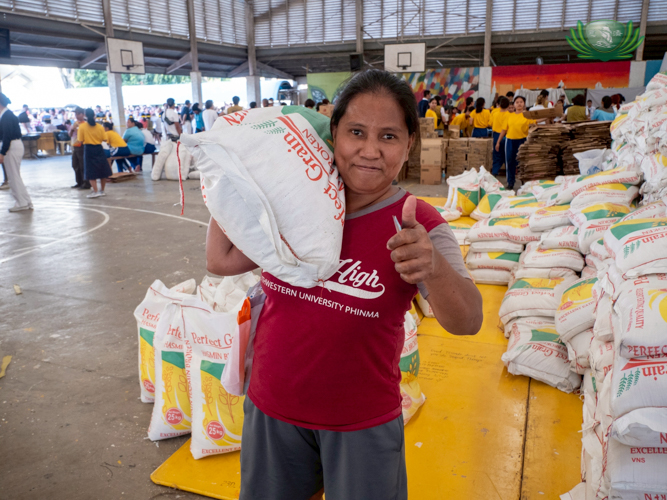 Lorina Caño shows her strength and smiles with a thumbs-up while carrying a 25-kg sack of rice.
