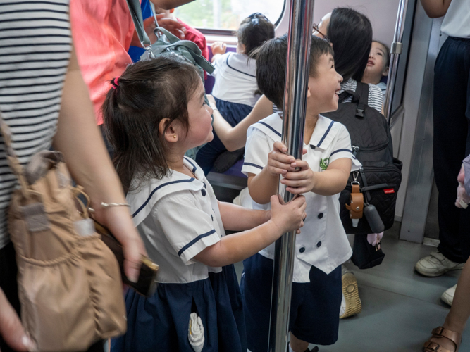 Following safety instructions, preschoolers grip the handrails while their parents maintain watchful eyes during the train ride.