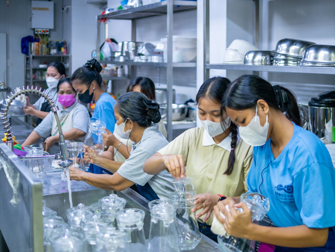 Volunteerism knows no age: Tzu Chi scholars (in blue) and beneficiaries training to be caregivers (in brown) help out in the kitchen. 【Photo by Daniel Lazar】