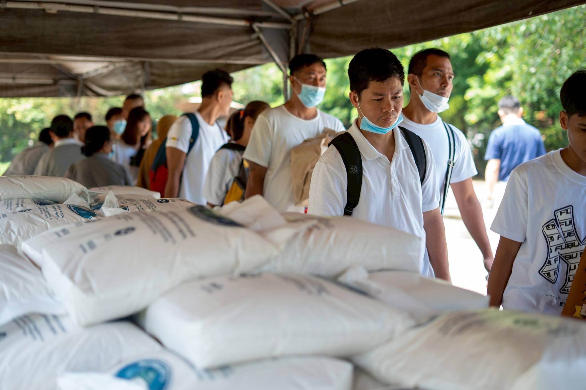 Medical assistance beneficiaries line up to claim two sacks of 10 kg rice and a bag of assorted groceries. 