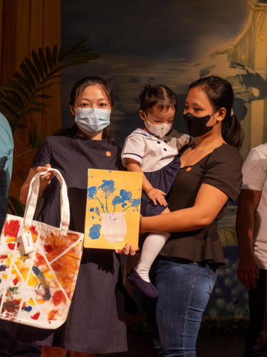 Mom Michelle Fang holds up artwork and a hand-painted tote bag made by her daughter Olivia. 【Photo by Jeaneal Dando】