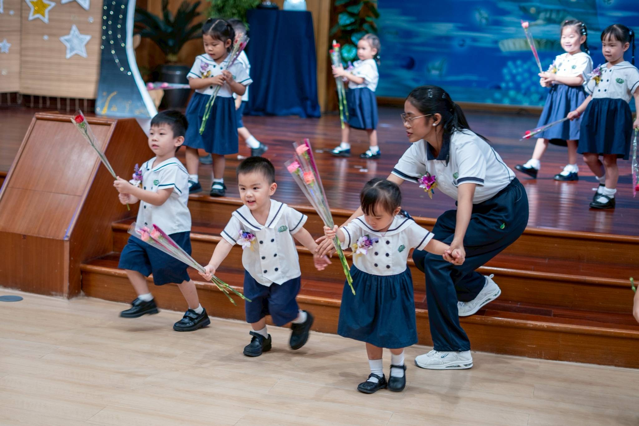 Teacher Tine Udarbe helps nursery students down the stage as they excitedly offer flowers to their parents. 