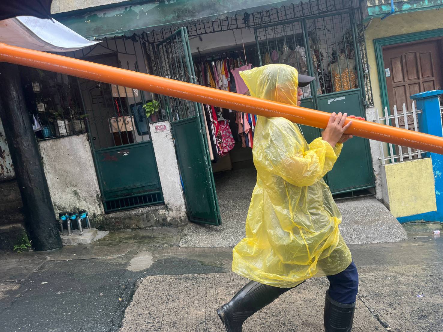 Under pouring rain, a Tzu Chi staffer carries a PVC pipe to the home of Tech-Voc scholar Irene Labra.