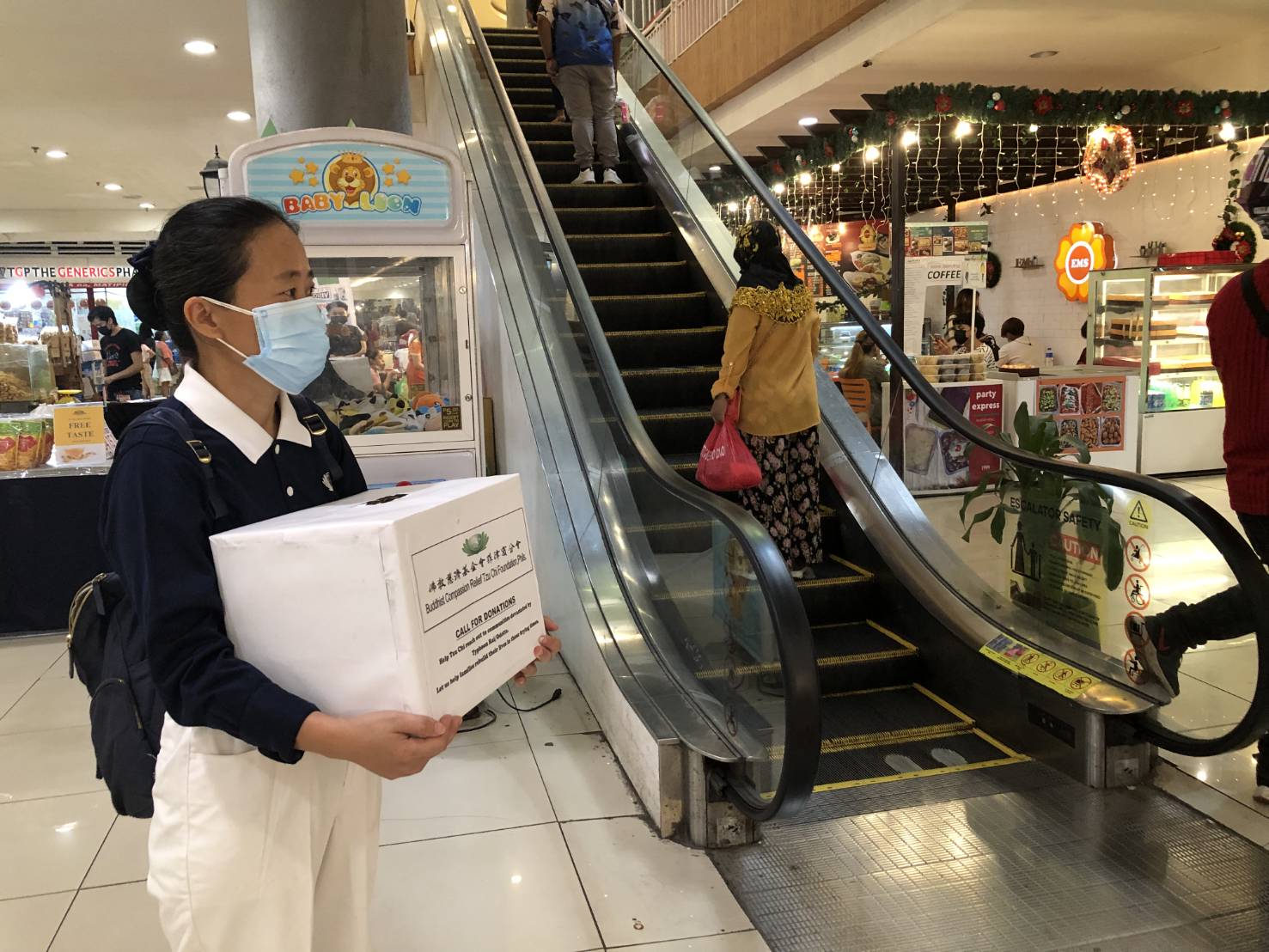 A volunteer waits patiently for shoppers by an escalator. 