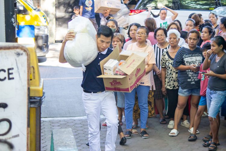 Customers watch as a Tzu Chi volunteer carries a sack of clothing and a box of products to be sold at the bazaar. 【Photo by Marella Saldonido】