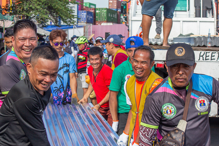 Local volunteers and residents of Isla Puting Bato joyfully work together in carrying the GI sheets under the heat of the sun. 【Photo by Marella Saldonido】