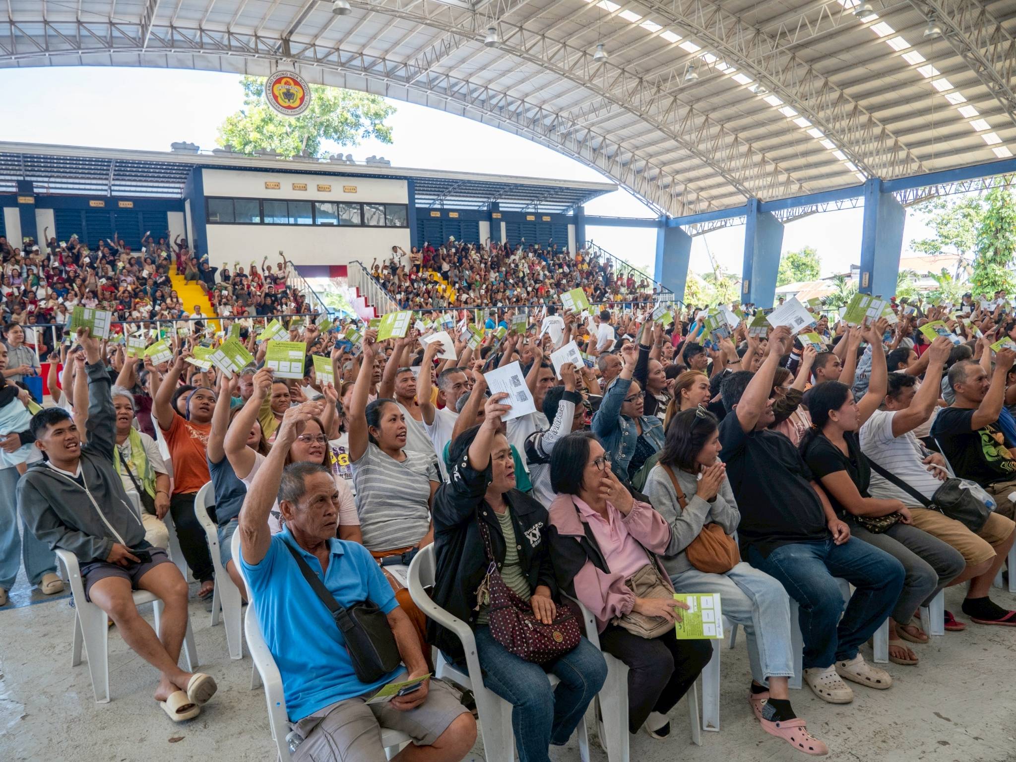 Beneficiaries of Typhoon Basyang gratefully raise their family card coupons before claiming their grocery gift check.