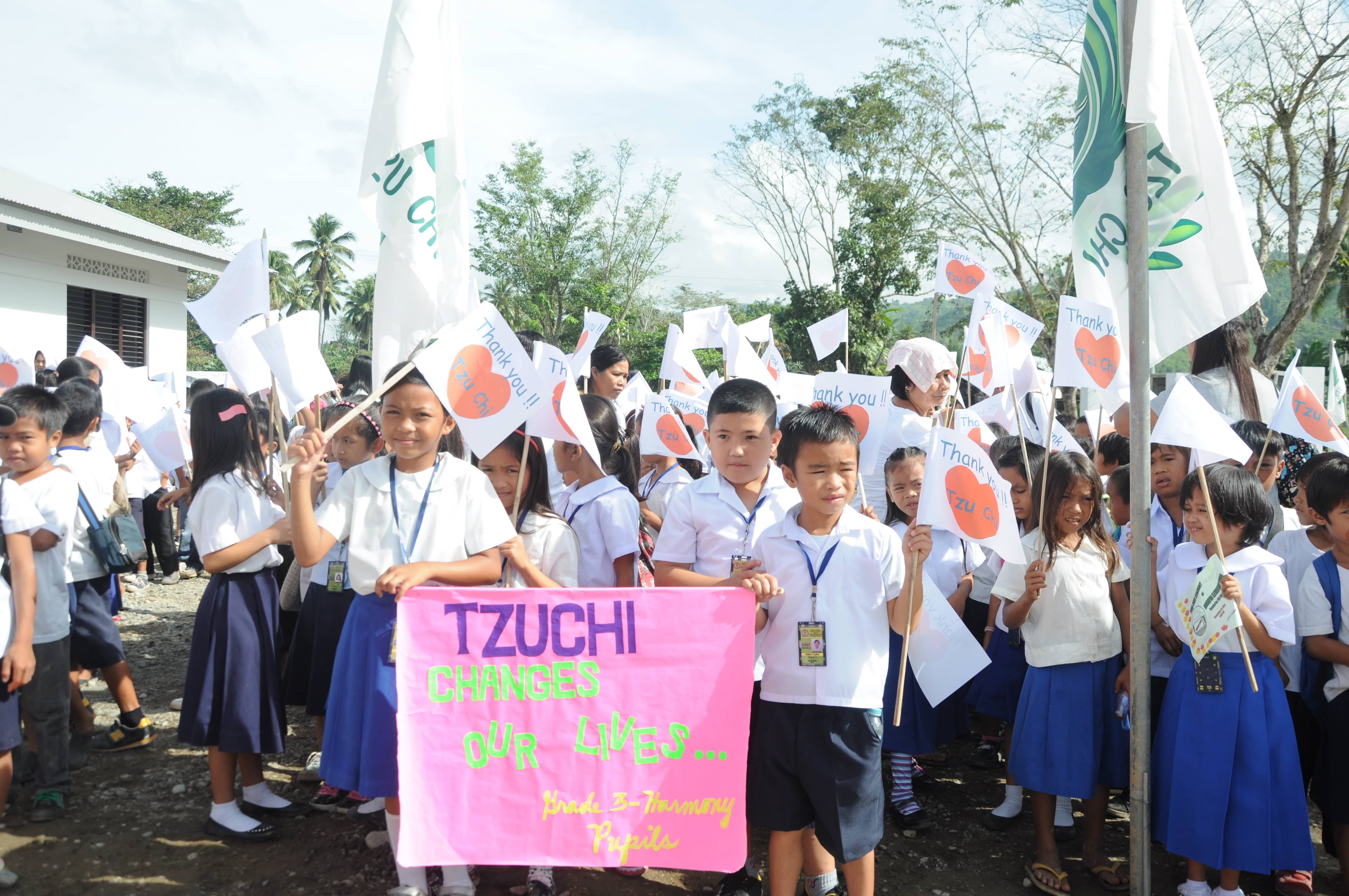 Mangayon Elementary School’s Grade 3 students wave their banner and flags to welcome Tzu Chi volunteers during the turnover ceremony of their rebuilt school on December 1, 2014.