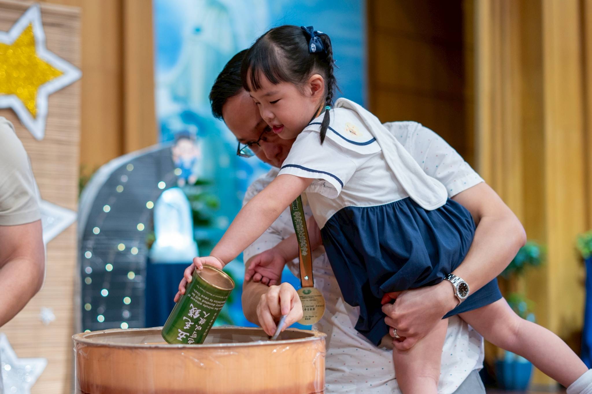 After receiving their certificate, preschoolers drop their coin bank donations in a large bamboo bank.