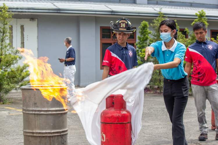 Tzu Chi scholars and their parents participate in a simulated fire training exercise. Here, they use a wet blanket to extinguish fire from a gas tank. 【Photo by Marella Saldonido】