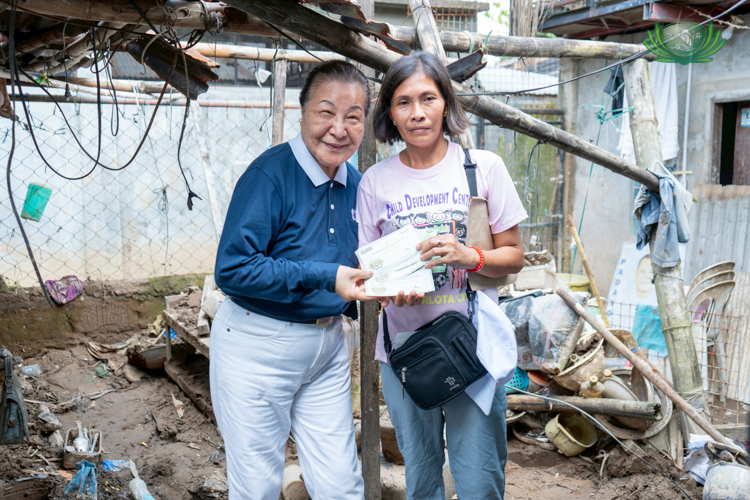Tzu Chi volunteer Siu Siu (Lee-Ching Lu) poses with Edsie Malaga while she receives a grocery voucher. They stand on what was once Edsie’s home, now filled with mud and debris brought by the flood.