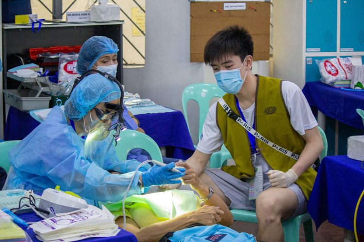Carl Francis Chua, son of Tzu Chi volunteer Nelson Chua, assists in a dental procedure. It was through him that his teammates learned about Tzu Chi’s 246th medical mission. 【Photo by Marella Saldonido】