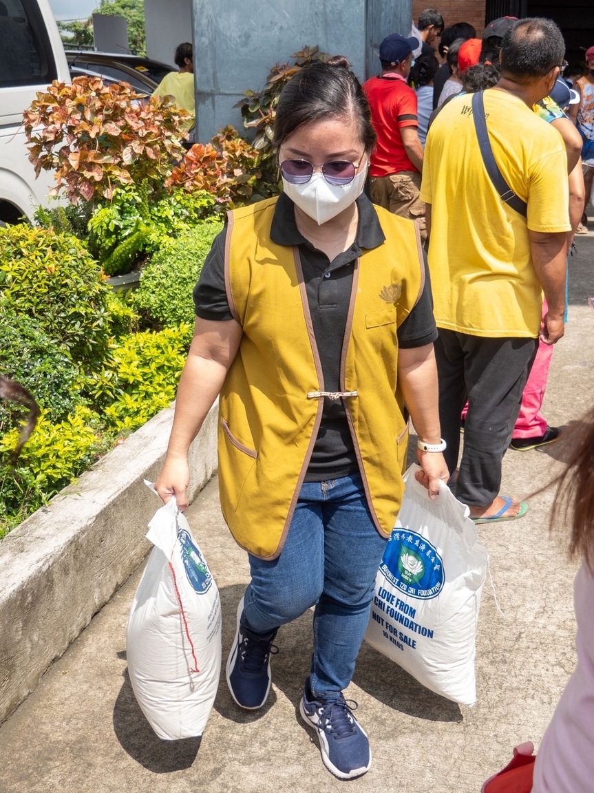 Volunteer Angge Salva thanks beneficiaries in the exit area of the stadium, and helps the elderly and people with children carry their heavy sacks of rice. 