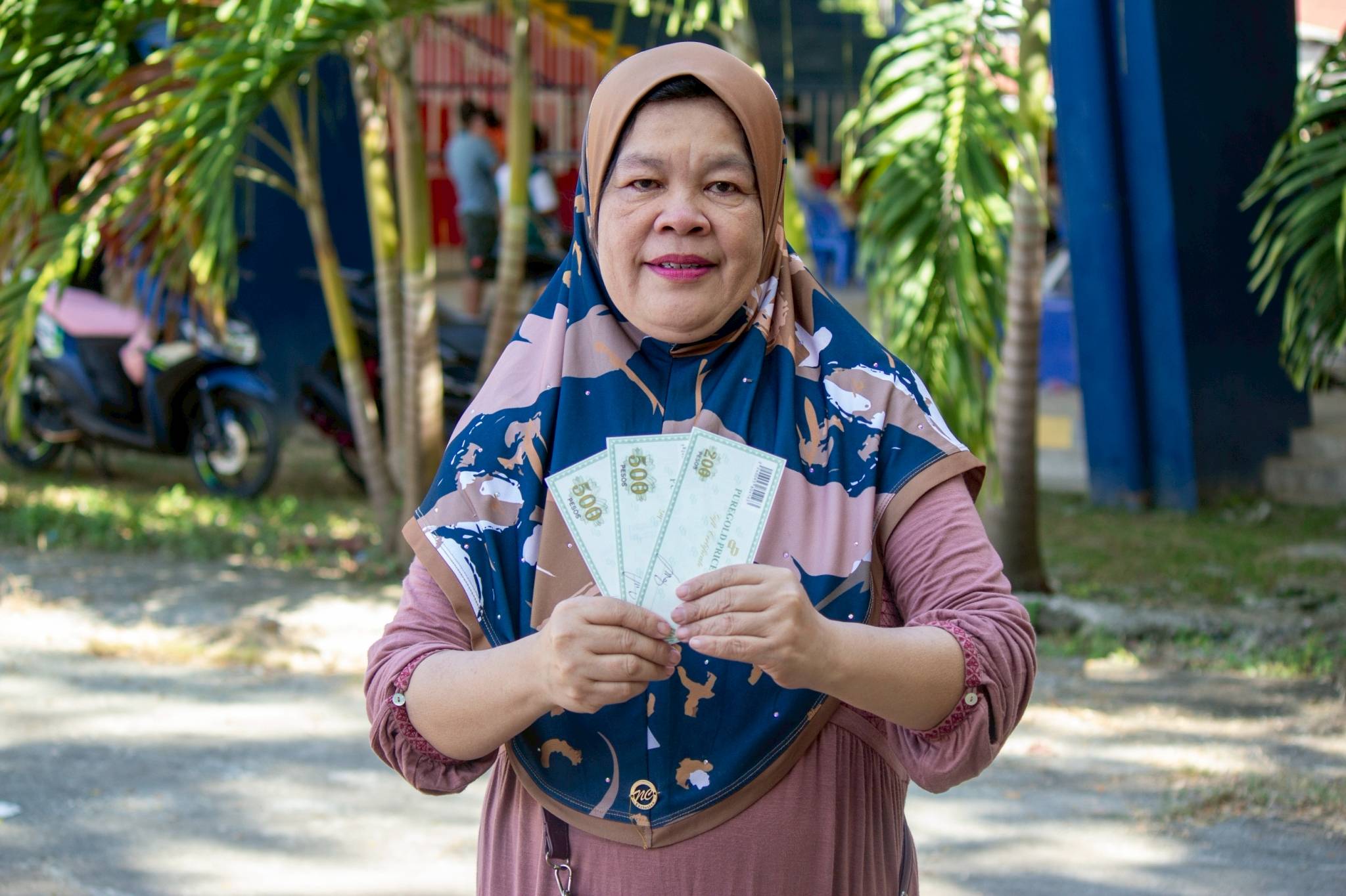 Beneficiary Farida Malik of Barangay Mahayahay poses with her gift checks, noting that beyond the aid, she values the organized and respectful relief distribution process.