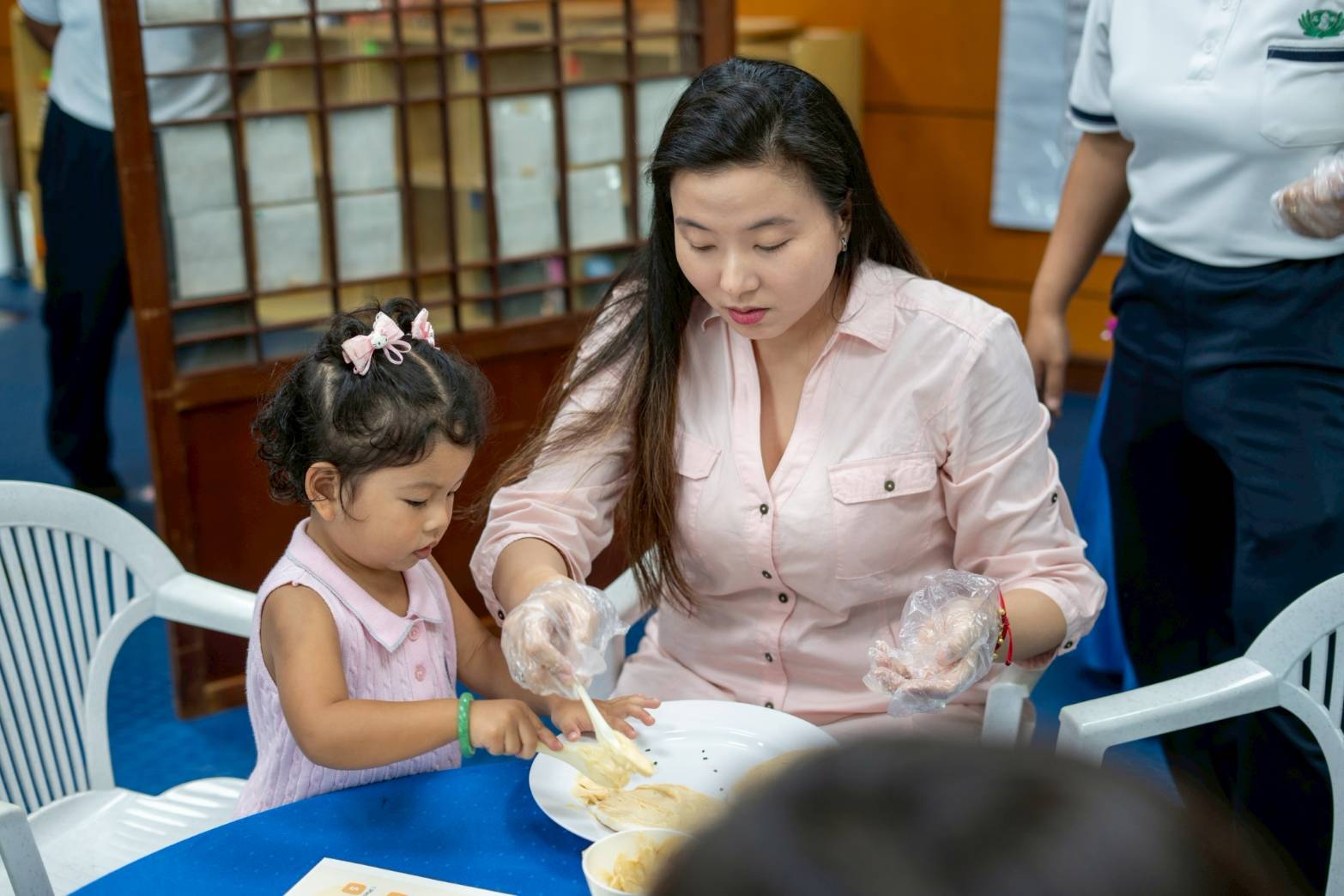 Charmeuse Lee and child Chloe are focused on adding cream on their pizza dough showing  teamwork together. 