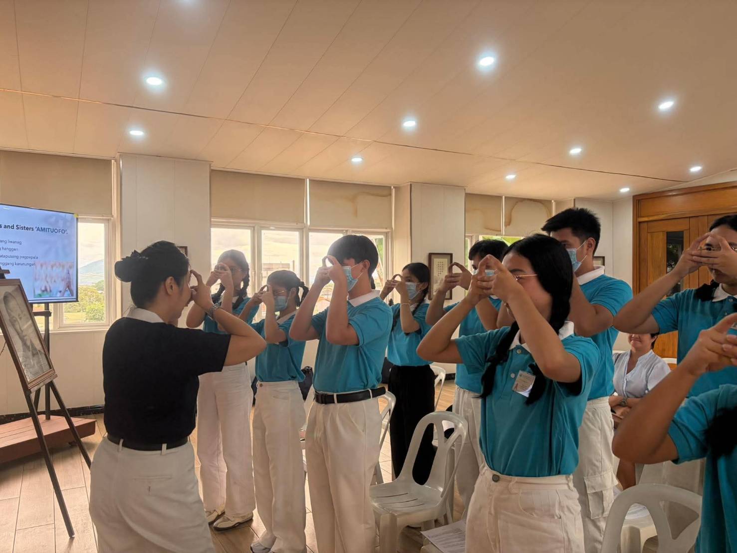 In Tzu Chi Pampanga, Tzu Chi volunteer Pansy Ho guides 32 scholars in making the hand sign for “Amituofo,” a Buddhist greeting that translates to “infinite light.”