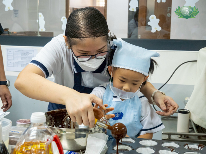 Tzu Chi Great Love Preschool Philippines Directress Jane Sy guides a young learner on how to transfer the cupcake batter into the trays. 