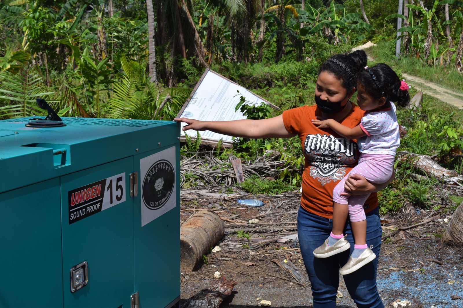 With her daughter in her arms, Maricar Ligones checks out the 15kVA generator that has restored water to Barangay Canangkaan in Corella. 