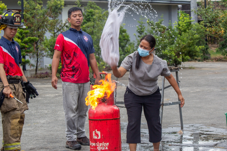 Tzu Chi scholars and their parents participate in a simulated fire training exercise. Here, they use a wet blanket to extinguish fire from a gas tank. 【Photo by Marella Saldonido】