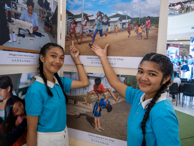 Sisters and Tzu Chi scholars Aleza (left) and Espiranza Obinguar, 17 and 19, respectively, pose next to a photo of themselves running at the grounds of the Palo Great Love Village 10 years ago. 【Photo by Matt Serrano】