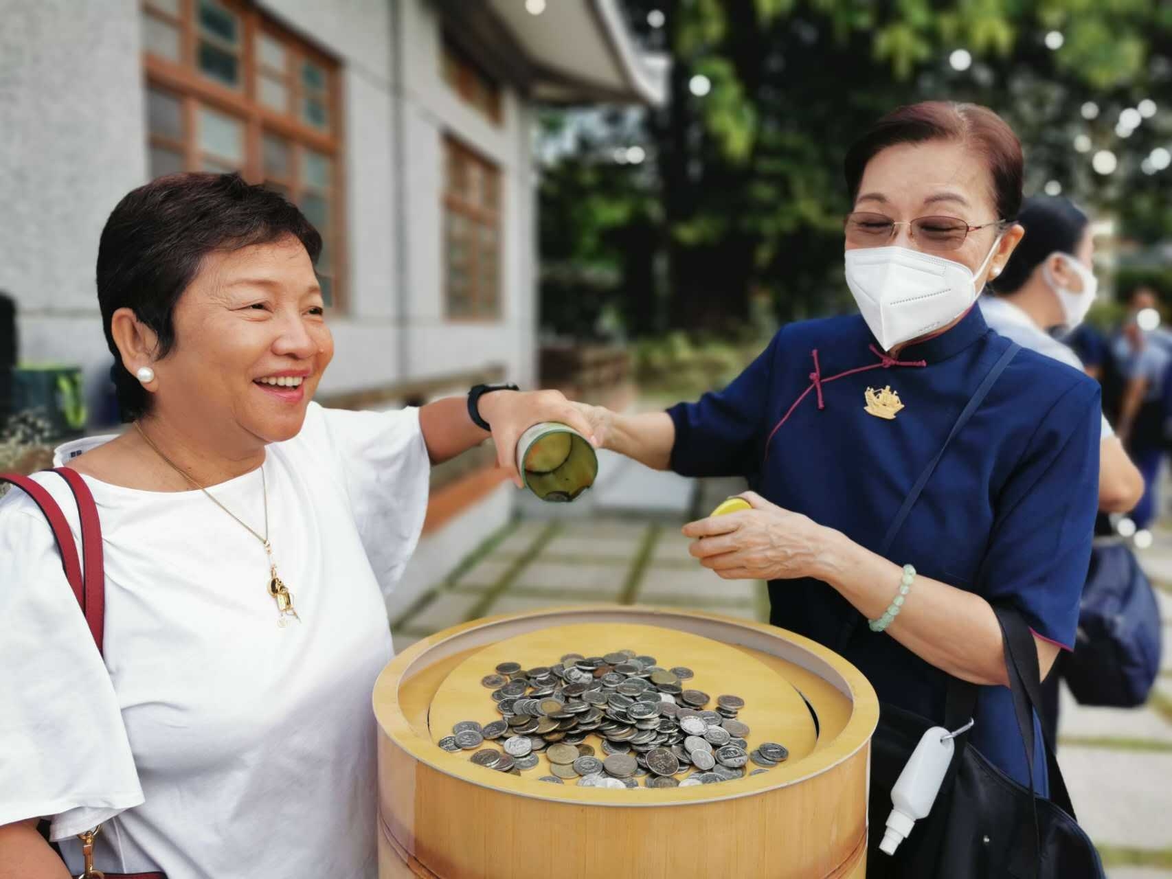  A volunteer helps a guest transfer her coin bank offerings.