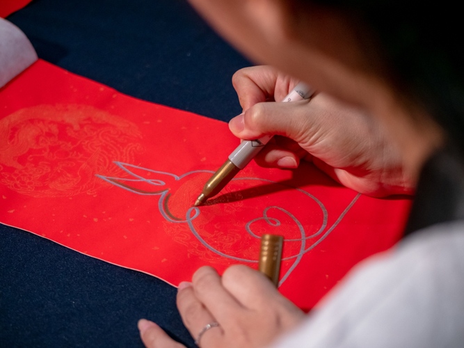 Artist Cindy Siy draws a rabbit on red paper before an artist enhances it further with Chinese calligraphy.【Photo by Daniel Lazar】