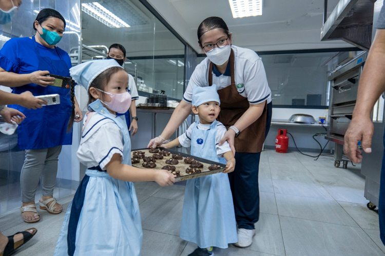 School directress and volunteer Jane Sy encourages the students to place the shaped cookie dough in the pre-heated oven with utmost safety and guidance.
