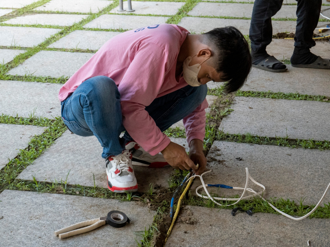 A volunteer embeds wires on the ground to provide electricity for the bazaar’s outdoor setup【Photo by Matt Serrano】