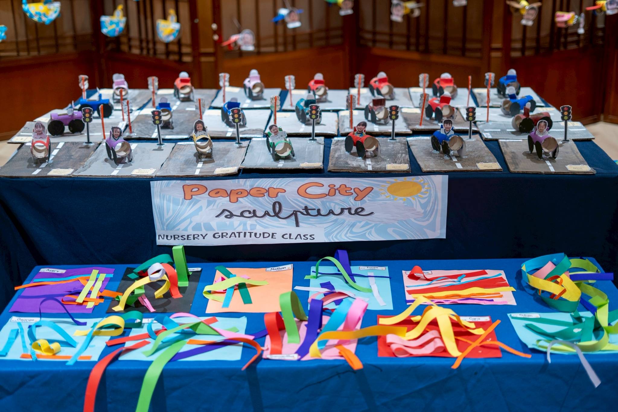 Nursery students affixed photos of their faces on paper sculptures of submarines, cars, planes, and hot air balloons.