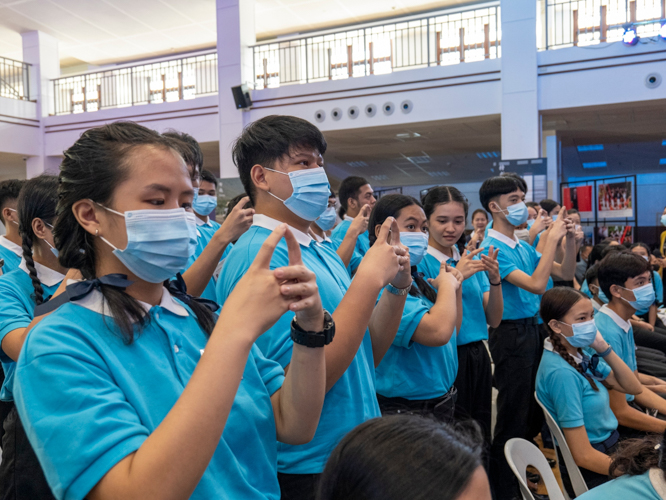 In a fun game on Tzu Chi etiquette and general knowledge, scholars demonstrate the hand gesture for the greeting “Amituofo.”