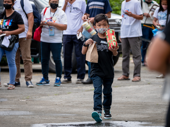 A young boy picks up a gift and bag of medicines. 【Photo by Daniel Lazar】