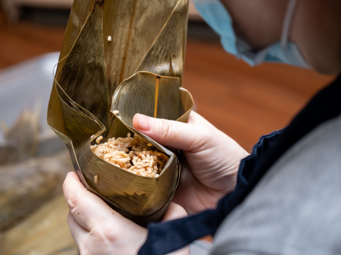 A volunteer carefully wraps the sticky rice into bamboo leaves, ensuring it isn't too tight or the machang will burst open when cooked.【Photo by Daniel Lazar】