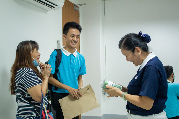 Edrian Delos Reyes (center) and his mother Felicitas (left) turn over a coin can donation to Tzu Chi Education Committee volunteer Rosa So (right). 