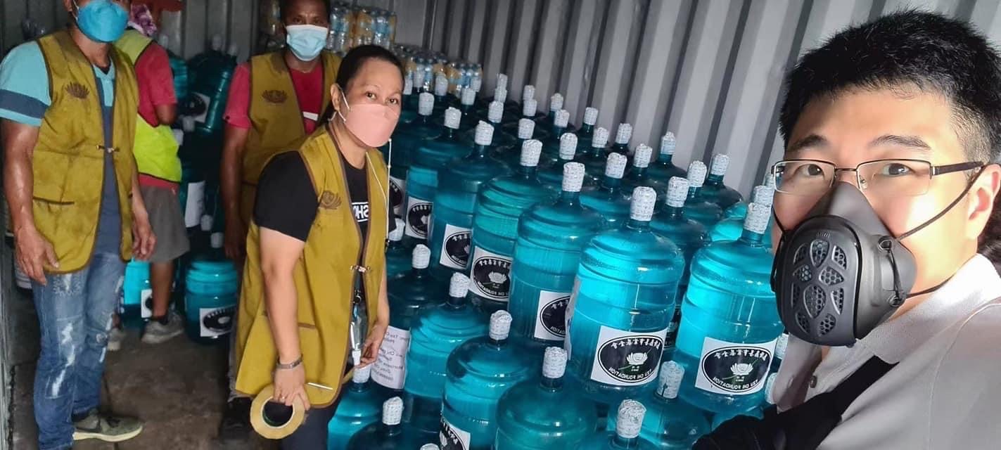 Volunteers pose for a selfie before the stacks of donated drinking water. 
