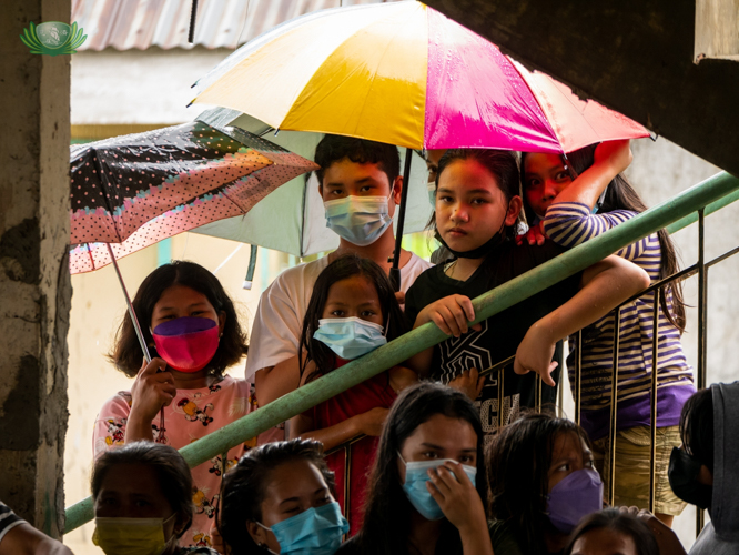 Young beneficiaries take cover under umbrellas during a visit from Tzu Chi volunteers on a rainy day.
