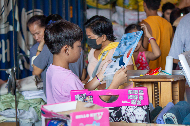 A young boy reads a book he picked up among the random items at the bazaar. 【Photo by Marella Saldonido】