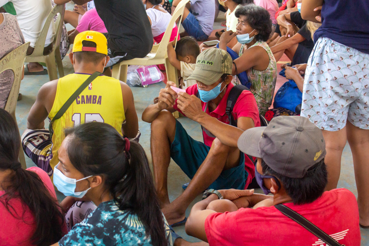 Recipient inspecting his relief ticket, while waiting with other recipients for the relief distribution to start.【Photo by Mavi Saldonido】