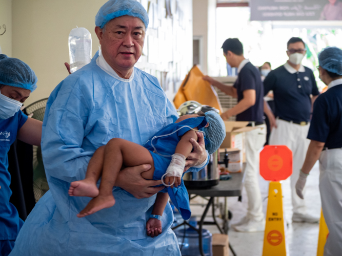 TIMA pioneer Dr. Jo Qua carries a child patient from the operating room to the Post-Anesthesia Care Unit. 【Photo by Daniel Lazar】