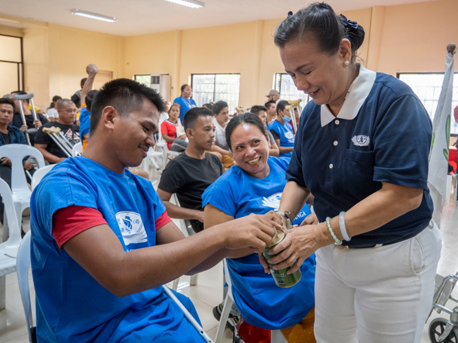 A prosthesis recipient smiles as he places his donation in the coin can.