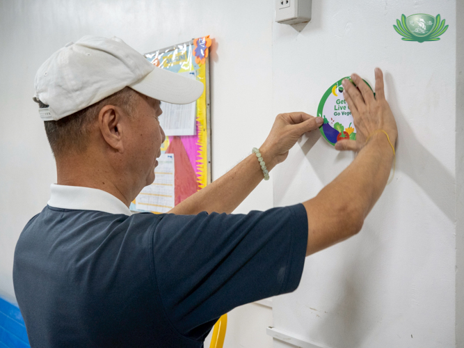 Tzu Chi volunteer Luis Diamante places a “Go Vegetarian” sticker on a school’s bulletin board.