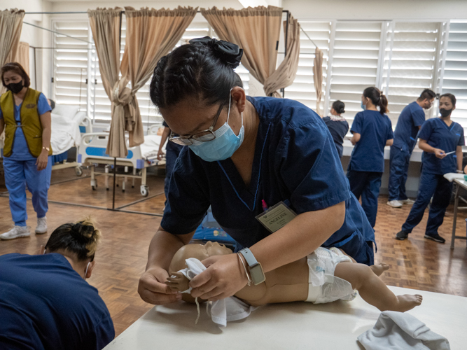 Angeline Gilboy conducts a practice session of dressing a newborn baby in their caregiving class. 【Photo by Matt Serrano】