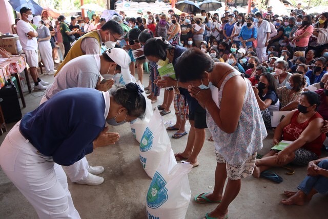 Volunteers and beneficiaries bow before each other as the latter receives their rice aid.
