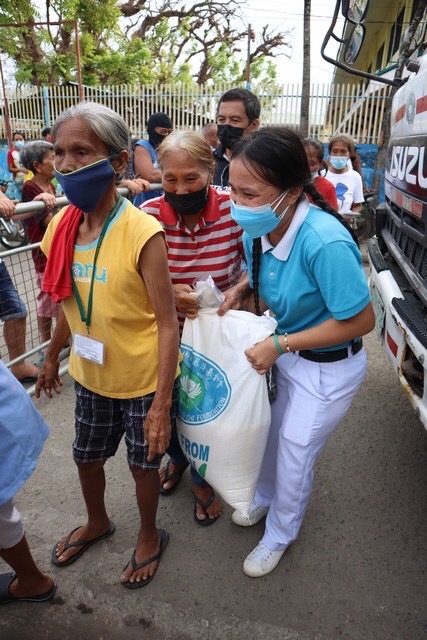 A Tzu Chi youth volunteer helps a senior citizen carry her rice relief.