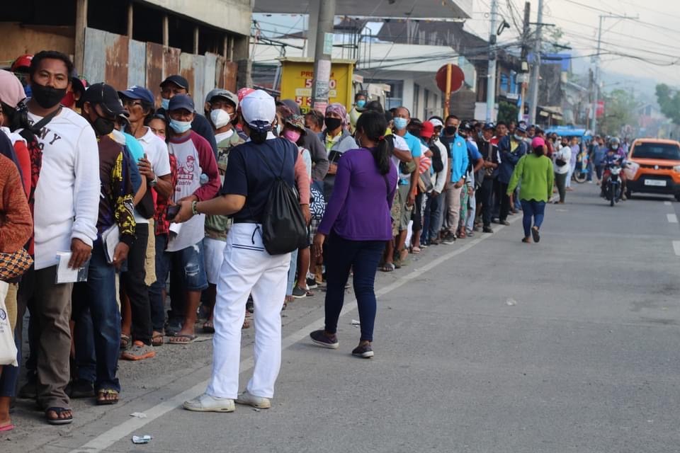 A volunteer keeps beneficiaries in an orderly line as they wait to claim their cash assistance at Metrobank Sogod Branch, Southern Leyte.